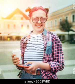 Magnifique moderne jeune femme adolescent Portrait avec une coiffure extraordinaire dans une chemise à carreaux avec capuchon « coffee to Go » et smartphone mince. Moderne te Banque D'Images