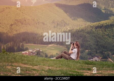 Une fille avec un appareil photo est assise sur une colline et des photos de montagne. Jour d'été Banque D'Images