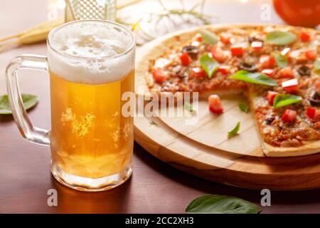 Verre de Chopp délicieuse pizza aux olives et pepperoni râpé sur planche de bois, amis autour de la table Banque D'Images