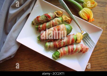 Des courgettes grillées enveloppées dans un bacon sur une plaque blanche Banque D'Images