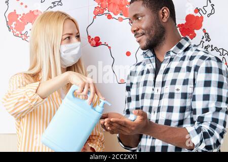 Portrait de deux personnes diverses, la femme caucasienne donner un spray pour la désinfection des mains à un type africain. Se protéger de COVID-19, utiliser des antiseptiques. Moût Banque D'Images