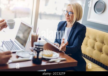 femme d'affaires réussie partageant ses secrets d'affaires. gros plan vue de côté. charmante femme senior parlant avec un client dans le café Banque D'Images