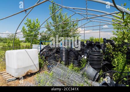 Réservoir de stockage en plastique avec insecticide liquide, clôture en treillis métallique et conteneurs en plastique noir dans la zone de stockage de l'exploitation commerciale de serre. Banque D'Images