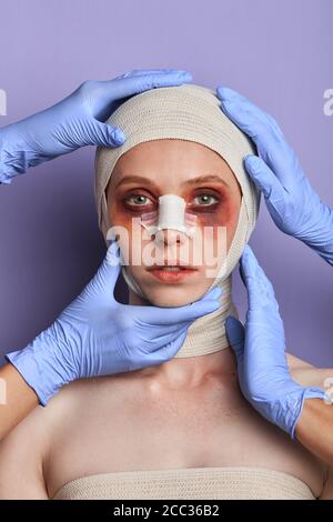 médecins en gants touchant le visage du patient, en le vérifiant, en préparant le visage pour le traitement. portrait en gros plan, arrière-plan bleu isolé, prise de vue en studio Banque D'Images