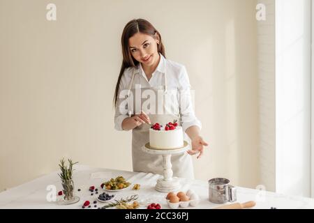 souriante charmante femme chef regardant l'appareil photo tout en décorant le gâteau, photo de gros plan Banque D'Images