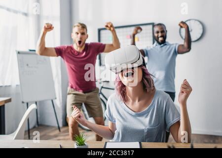 Mise au point sélective d'une femme d'affaires dans un micro-casque vr montrant un geste oui avec des collègues multiculturels à l'arrière-plan Banque D'Images
