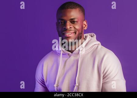 Athlète africain souriant à l'appareil photo, prêt pour le sport avec un sweat-shirt à capuche blanc isolé sur fond violet. Banque D'Images