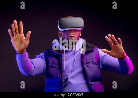 Boxeur professionnel africain en tenue violette décontractée regardant à travers la compétition avec sa participation, en utilisant des lunettes VR, étudiant des erreurs et des cactus Banque D'Images