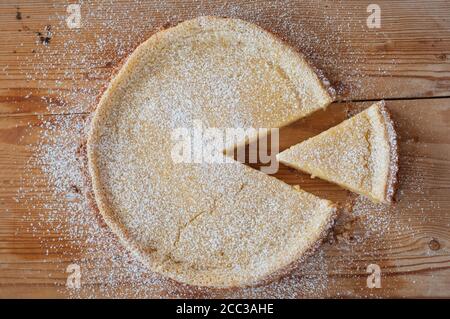 Vue de dessus photo d'une tarte à la pâtisserie avec sucre en poudre et une tranche séparée sur fond de bois. Banque D'Images