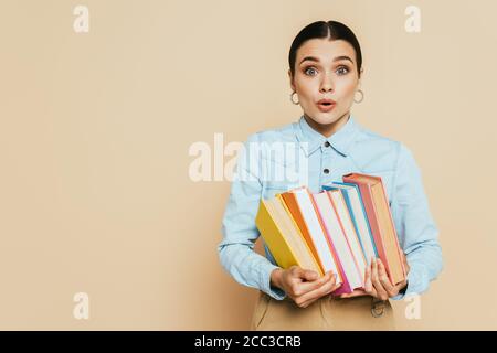 élève choqué dans une chemise en denim avec des livres sur le beige Banque D'Images