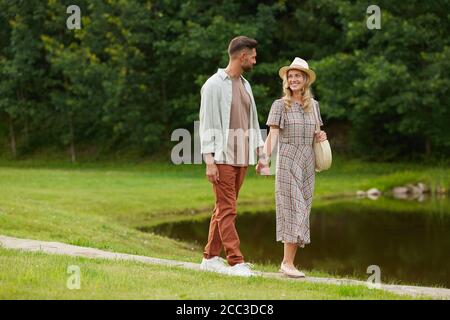 Portrait complet d'un couple adulte romantique tenant les mains tout en marchant au bord du lac dans un paysage rustique, espace de copie Banque D'Images