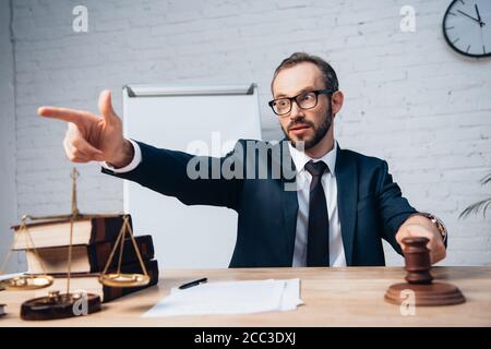 attention sélective du juge barbu dans les lunettes pointant avec le doigt et tenir le bavette près des papiers sur la table Banque D'Images