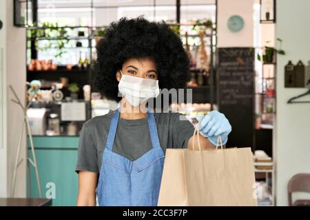 Femme africaine américaine de café travaillant avec un masque facial tenant un sac de nourriture à emporter. Banque D'Images