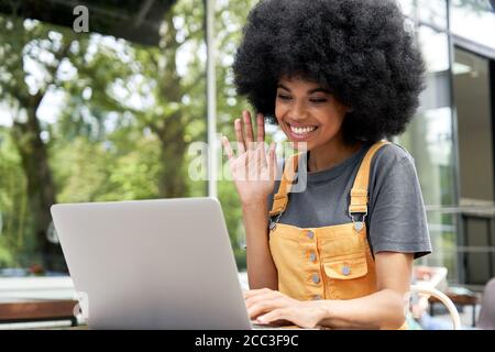 Une fille africaine heureuse utilisant un ordinateur portable de vidéoconférence appelant un ami dans un café extérieur. Banque D'Images