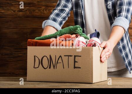 vue rognée de l'homme tenant une boîte en carton avec lettrage de don et des vêtements sur fond de bois, concept de charité Banque D'Images