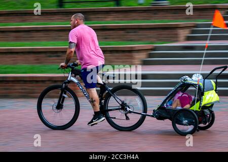 Maryland, Etats-Unis 08/14/2020: Un jeune homme caucasien portant un t-shirt rose et un short bleu est de monter son vélo de montagne avec une remorque enfant . Il a le wirel Banque D'Images