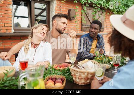 Groupe de jeunes très beaux appréciant dîner à l'extérieur tout en s'asseyant à une table en bois au bord d'un cottage, espace copie Banque D'Images