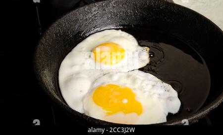 œufs de poulet, œufs frits dans une poêle en fonte, petit déjeuner, omelette, deux œufs avec jaunes sont frits sur la cuisinière. Banque D'Images