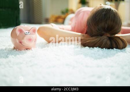 Gros plan sur une femme avec une tirelire tout en posant sur un tapis blanc dans la maison par beau temps. Banque D'Images