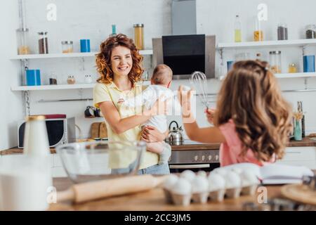 vue arrière de la fille montrant l'œuf de poulet et fouetter à la mère avec son bébé, foyer sélectif Banque D'Images