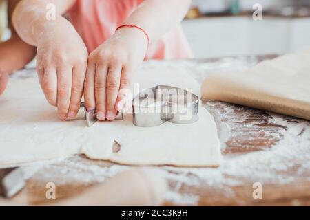 vue rognée de l'enfant coupant des recettes de la pâte roulée sur la table parsemée de farine Banque D'Images