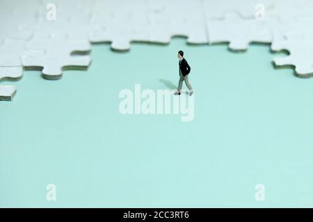 Photo conceptuelle de la stratégie d'affaires - petit homme d'affaires marchant devant de puzzle Banque D'Images