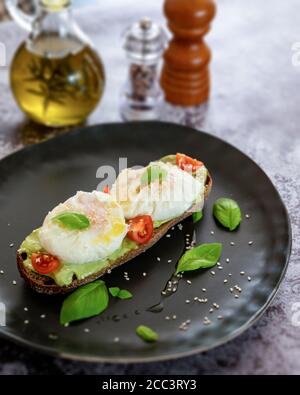 Purée d'avocat sur une assiette noire avec tomates aux œufs pochés Et les feuilles de basilic Banque D'Images