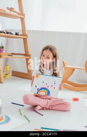 fille en pyjama assise sur le sol et montrant le dessin près feutres multicolores Banque D'Images