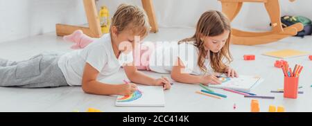 concentré frère et soeur en pyjama couché sur le sol et dessin avec des stylos feutres dans des carnets d'esquisses Banque D'Images