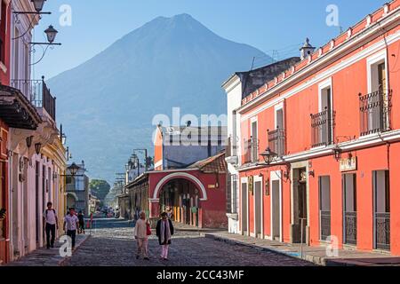 Volcán de Fuego et touristes occidentaux marchant dans la rue avec des maisons coloniales colorées dans la ville Antigua Guatemala, département de Sacatepéquez, Guatemala Banque D'Images