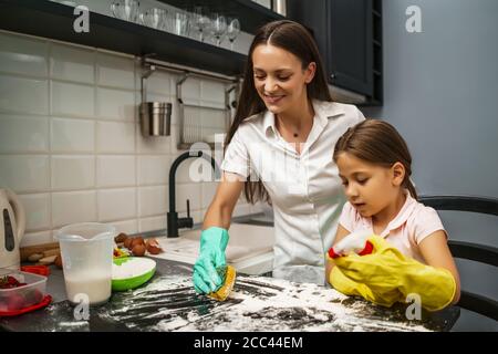 La mère et la fille nettoient la table dans la cuisine après avoir fait des biscuits. Banque D'Images