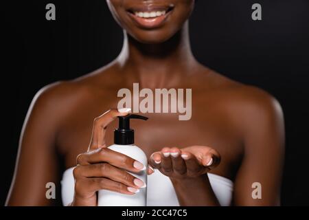 vue rognée d'une femme afro-américaine appliquant une lotion pour le corps isolé à la main sur le noir Banque D'Images