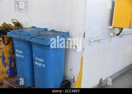 Les poubelles en plastique bleu pour les déchets alimentaires fermement fixées aux rails sont situées derrière la superstructure du conteneur de cargaison. Banque D'Images