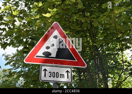 Panneau de signalisation rouge en triangle rouge, tombant des rochers de la droite, sur la route secondaire entourée d'arbres dans les collines au-dessus de la ville de Fribourg. Banque D'Images