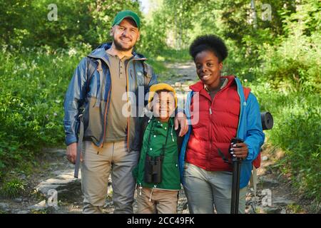 Portrait d'une famille heureuse de touristes debout dans la forêt et sourire à l'appareil photo Banque D'Images