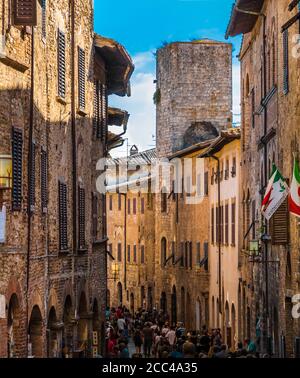Belle vue sur la via San Giovanni, la rue principale de la petite ville médiévale fortifiée de la colline San Gimignano, Toscane, Italie. Les touristes sont en marche à travers... Banque D'Images