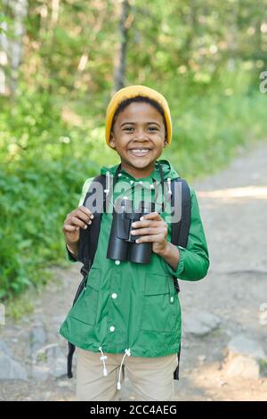 Portrait d'un garçon africain heureux tenant des jumelles et souriant caméra dans la forêt Banque D'Images