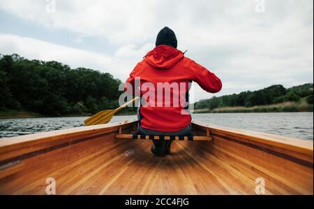 Vue arrière de l'homme en canot de pagayage de veste rouge jour nuageux Banque D'Images