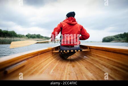 Vue arrière de l'homme en canot de pagayage de veste rouge jour nuageux Banque D'Images