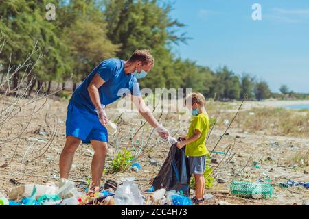 Volontaires dans le masque bleu. Père, fils ramasser les ordures qui polluent la plage près de la mer de lazur. Problème de pollution de la planète par les déchets déversés Banque D'Images