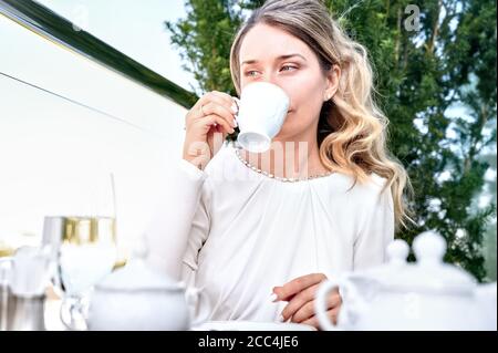 Triste femme buvant une tasse de café. Blonde fille en robe blanche. Portrait en extérieur Banque D'Images