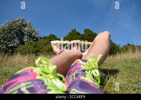 Jeune femme qui s'étend sur l'herbe avec les jambes étirées Banque D'Images