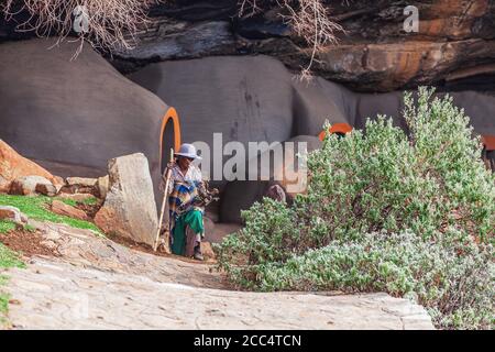 BEREA, LESOTHO - le 23 août 2012 : femme autochtone en face de troglodytes faits de boue dans le district de Berea, Lesotho Banque D'Images