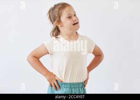 Petite fille avec le syndrome de Down dans les vêtements décontractés debout contre le fond blanc Banque D'Images