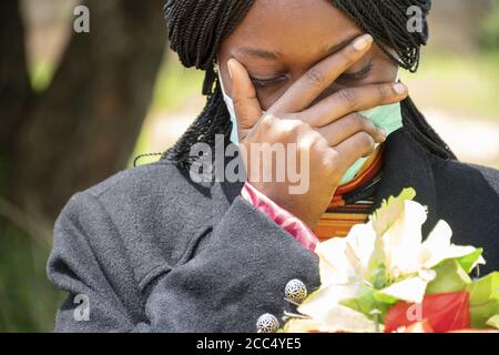 La jeune femme noire pleure, portant un masque et tenant des fleurs - le nouveau concept normal Banque D'Images