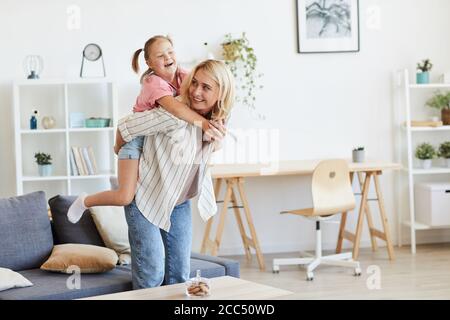 Mère à cheval sa fille avec le syndrome de Down sur son dos pendant qu'ils jouent dans le salon Banque D'Images