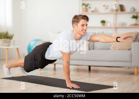 Homme souriant dans les vêtements de sport faisant des exercices pour les mains sur le tapis sur le sol Banque D'Images