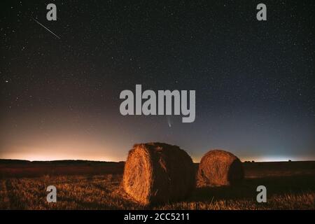 Meteor et Comet Neowise C2020 F3 dans Starry Sky de nuit au-dessus de Haystacks dans le champ agricole d'été. Étoiles de nuit au-dessus du paysage rural avec balles de foin Banque D'Images