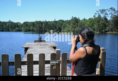 Femme Mestizo asiatique-africaine vue de côté prend une photo d'un lac. Banque D'Images