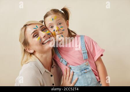 Portrait de la mère et de la fille heureux avec des visages peints embrassant les uns les autres et souriant à l'appareil photo sur fond blanc Banque D'Images